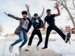 Three teenagers jumping on a sidewalk with snow on the ground