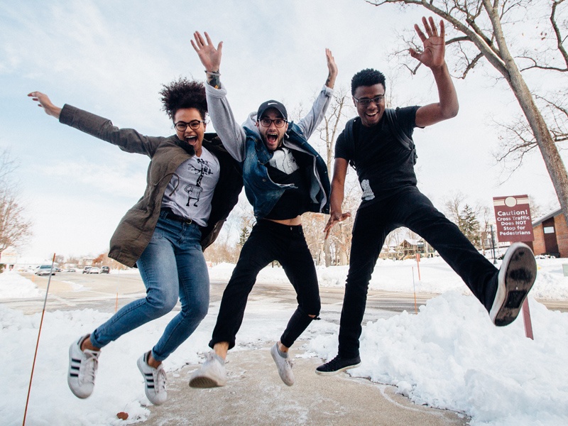 Three teenagers jumping on a sidewalk with snow on the ground